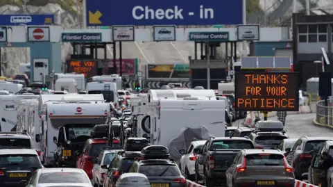 Cars queuing at a check-in point at the Port of Dover with an electronic sign saying 'Thanks for your patience'
