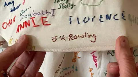 @LightninLex A pair of hands are holding a piece of fabric covered in embroided names. The one being held prominently to the camera is "JK Rowling"