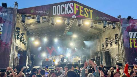 The main stage at Docksfest draped with banners as Razorlight perform, the crowd clapping and waving