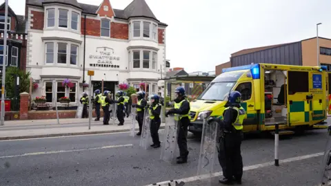 PA Media A line of police officers in riot helmets and shields stand in front of a pub.