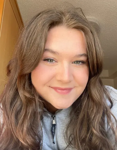 Anna Newbould A young woman with long, dark hair and a grey zip-up top