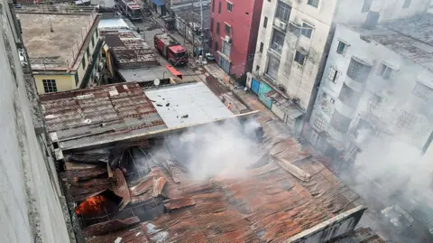 Getty Images White smoke billows from damaged tin roofs with flames visible underneath