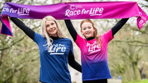 Cancer Research UK Gemma and her daughter Macy holding a Race for Life banner
