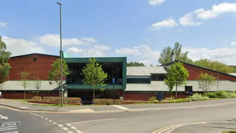 Farnham leisure centre. It is a brown building by a roadside, the sky is blue