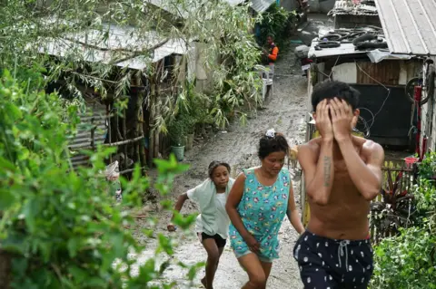 A boy covers his eyes, with two women behind him 