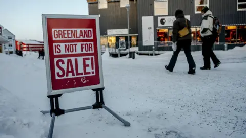 EPA/Shutterstock Persone camminano lungo una strada ghiacciata a Nuuk, la capitale della Groenlandia. Un cartello sulla strada dice: "La Groenlandia non è in vendita!"