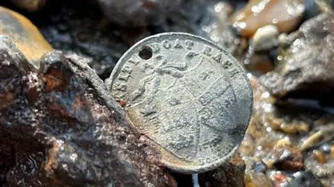 A rusty coin-sized medal with 'University Boat Race' on it, with the shield emblems of Oxford and Cambridge universities below