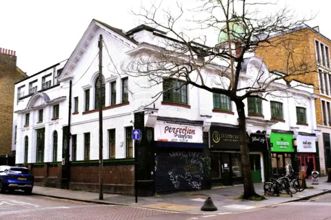 Historic England A white building on a street corner which has four modern shop fronts in its façade 