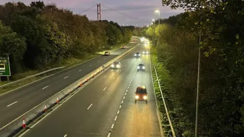 Landscape view of cars travelling on the A63 dual carriageway at dusk with the Humber Bridge in the distance