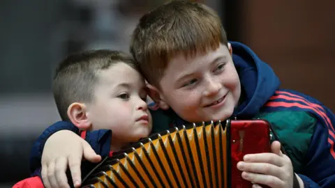 PA Media Two boys with dark hair hold an accordion and embrace