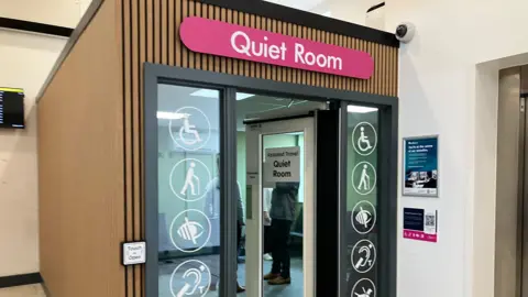 A glass room with various disability icons around the glass doors and a sign above saying "Quiet Room"