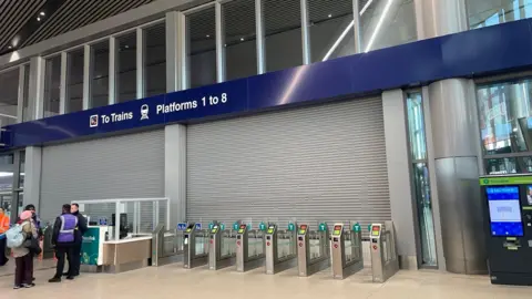 The shutters down at Grand Central Station's train platforms, there is people standing outside them.