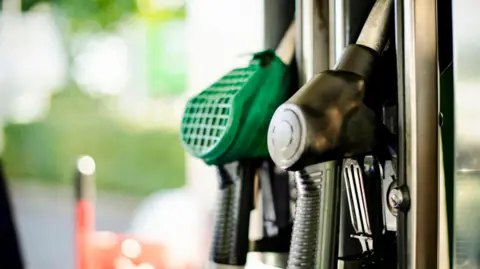 Getty Images Closeup of green and black fuel nozzles at a fuel station.