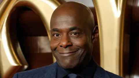 Reuters A close-up of Paterson Joseph attending the world premiere of Wonka at Royal Festival Hall, in London on 28 November 2023. He is smiling.