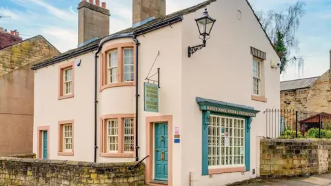 Maurice Dobson Museum An external view of the cream painted Maurice Dobson Museum and Heritage Centre. It's a two storey building on a corner with a blue painted door.