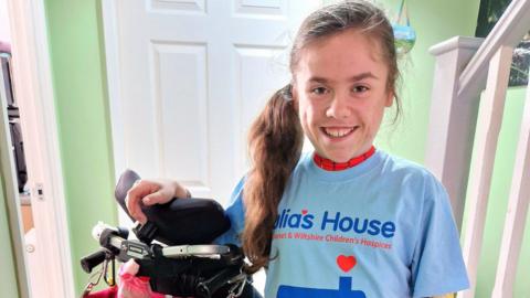 Carmela Chillery-Watson stood in her house, wearing a blue Julia's House t-shirt and stood next to her wheelchair