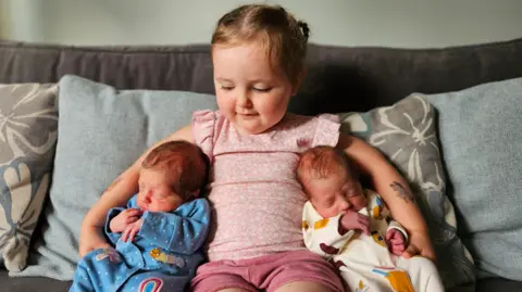 Emily Broughton Lottie with Isabelle and Phoebe under either arm, sitting on a sofa