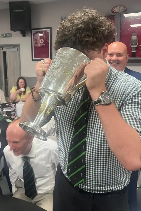 Caleb Tutt A man stood up drinking out of the silver cup