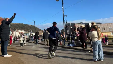 A wide shot of people skipping with large skipping ropes down the street by the coast.