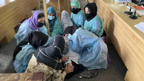 Afghan midwives in training attend to a woman lying on the ground