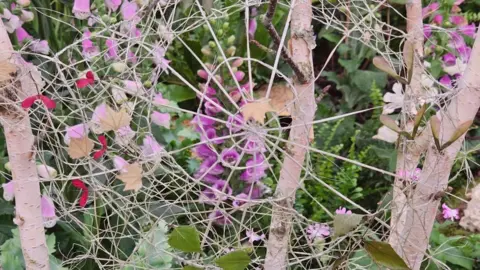 Relove Technology A spider-web like part of the sculpture with pink flowers and branches