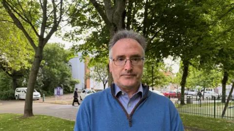 Patrick Lynch is pictured in Parade Gardens. He is wearing a blue jumper and has glasses