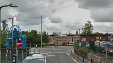 Google A silver car parked on a meter on a road with double yellow lines with a car park on the right