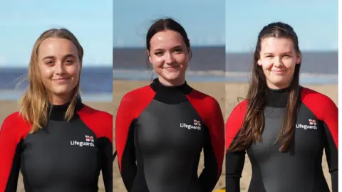 RNLI/Arun Gray Professional photos of RNLI lifeguards Lois Kemp, 25, Katie Roscoe, 21 and Effie Kennedy, 16, standing on the beach in lifeguards outfits and smiling into the camera