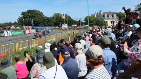 SOUTHERN 100 Spectators watch the racing from behind fencing as bikes race by.