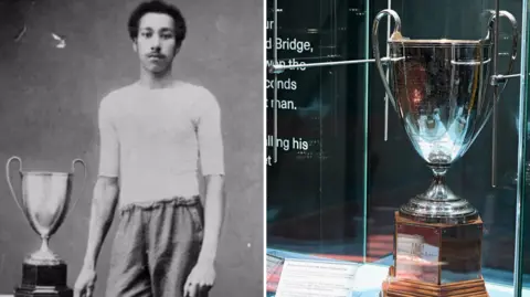 Arthur Wharton Foundation A composite image of Wharton with the Prince Hassan Pacha Cup, alongside the cup on display at the exhibition. On the left, a black-and-white image of Wharton standing with the trophy on a table beside him. He has short black hair and a moustache and wears a white top and shorts. On the right, a large silver cup with two handles trophy pictured in a glass cabinet.