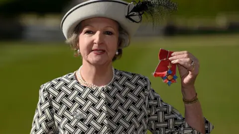WPA via Getty Images Penelope Keith being made a dame. She is dressed in black and white and holding up her medal for the cameras 