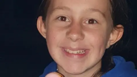 PA Media Ava, wearing a blue hoodie with her hair scraped back, smiles for the camera