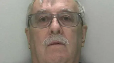 A man with a moustache and wearing glasses is pictured