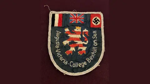 Bexhill Museum The Augusta Victoria College blazer badge which features an Union Jack, Swastika, a red and white lion rampant.