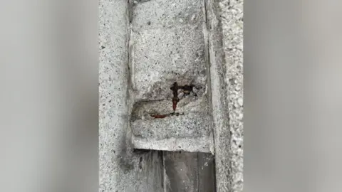 Church of the Good Shepherd A close up image of a section of structural concrete, showing where part of it has fallen away to expose the rusty metal framework beneath
