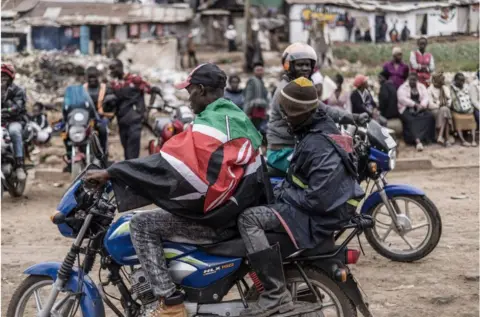 AFP A man on a motorcycle taxi with a Kenyan flag draped over him.