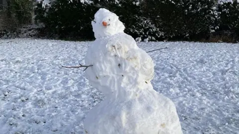 A wonky snowman leans slightly to the left in a field of snow