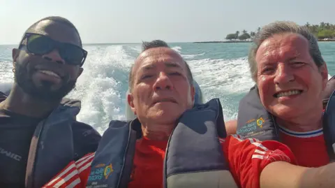 Albert Alfonso/Flickr Mosquera pictured on a speedboat next to Mr Alfonso, who is in the middle, and Mr Longworth, who is on the right. All three men are smiling at the camera and wearing life jackets. Spray from the speedboat can be seen on the water behind them.