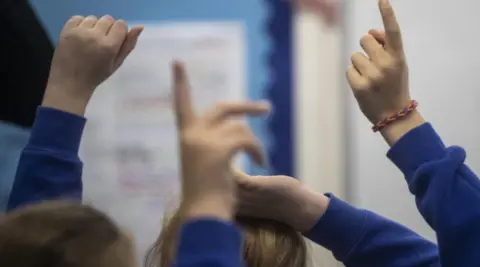  A generic image showing some children's arms in the air. They are wearing blue and their faces are not visible.