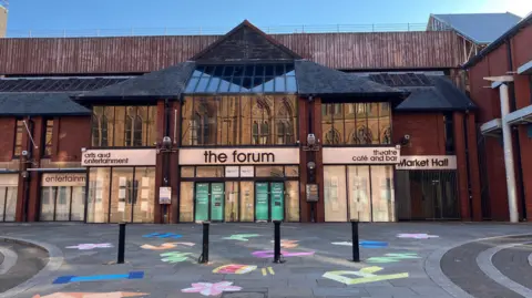 The Forum in Barrow, a large indoor space with a market and theatre. Signs above its glass doors read 'arts and entertainment', 'theatre', 'cafe and bar', and 'market hall'. The building closed earlier this year.