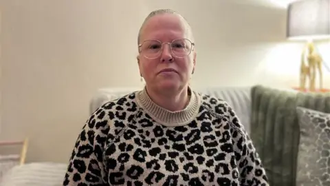 BBC Michaela pictured with her hair tied back looking at the camera. She is wearing glasses and a leopard print knitted jumper.