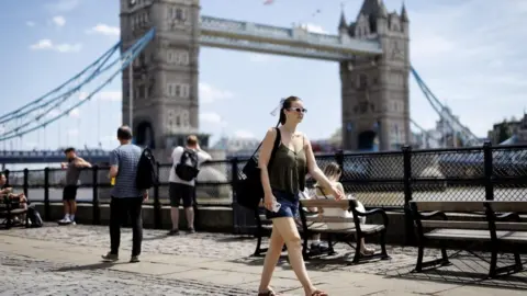 EPA/Shutterstock/Getty Images People near the River Thames during a warm day in London on 27 June 2025. A woman in shorts and a short sleeve top is at the centre of the image