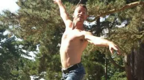 Karl Stevens Barechested Karl Stevens, jumps into a dancing pose in a garden