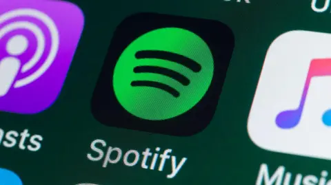 Getty Images Tampilan dekat layar ponsel yang menampilkan ikon aplikasi Spotify - lingkaran hijau berisi tiga garis hitam dengan latar belakang hitam.