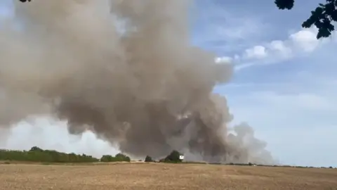 A large field fire. Thick smoke can be seen on the horizon. 
