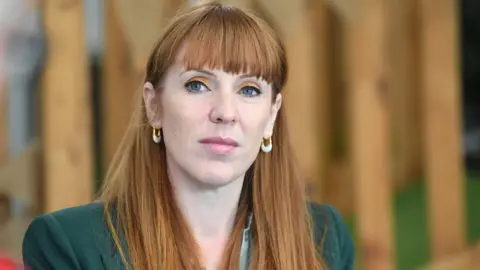 PA Media Image shows Angela Rayner, a Caucasian woman with red hair wearing orange eyeshadow and a green suit