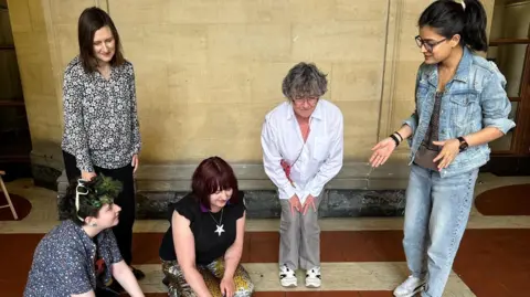 Anurita Chandola People are stood and kneeling around the patchwork near them and some are touching them