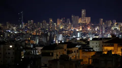 Reuters A night view of Beirut's illuminated downtown area, showing dense buildings and towering towers against a dark sky, after operations began between Israel and the Iran-backed group Hezbollah at 02:00 GMT. 