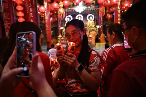 Lillian Suwanrumpha/AFP Seorang wanita berpose untuk foto dengan lilin menyala di sebuah kuil di Bangkok 