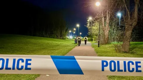 Leicester Media Police officers and tape at the intersection of two paths in an area of park land 